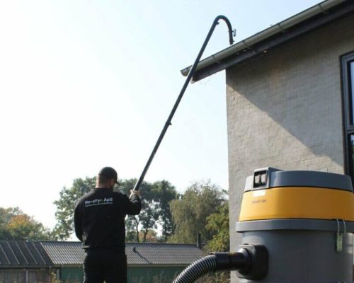 Mand fra RensFyn der renser tagrender med støvsuger på grå villa