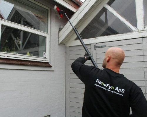 Medarbejder fra RensFyn i gang med at pudse vinduer på gråt hus med hvide vinduer